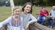 Two adopted girls having fun in the park with adoptive mum and dad in the background