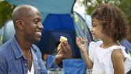 Black man and black girl picnic outside tent