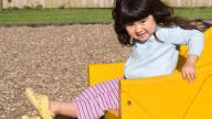 girl sitting in yellow playground toy